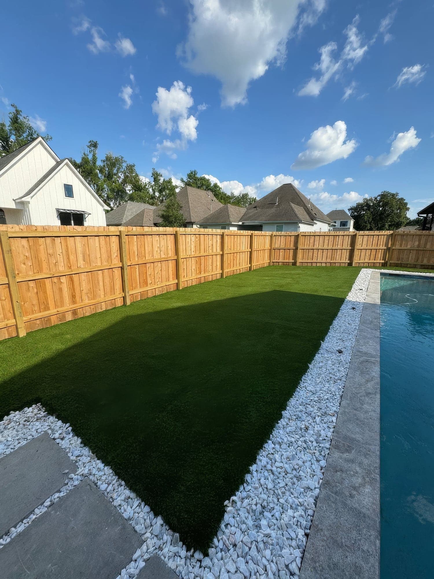 Artificial turf with white river rock edging beside a pool and a new cedar fence