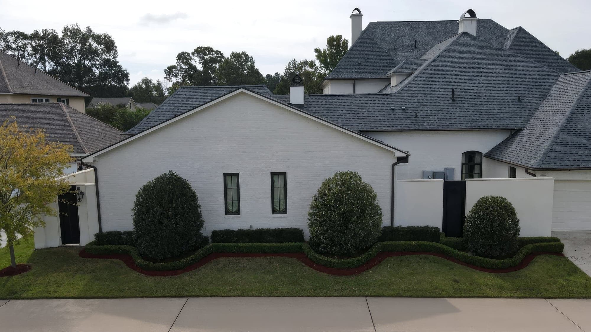 Aerial view of a white brick home with a wavy boxwood hedge border and fresh mulch beds